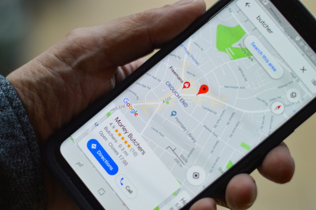 Hand holding a phone showing Google Maps with a local butcher search, map pins, and a business listing with ratings and Directions and Call actions